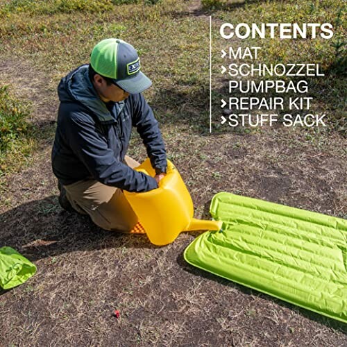 Person using an orange pump bag to inflate a green camping mat outdoors.