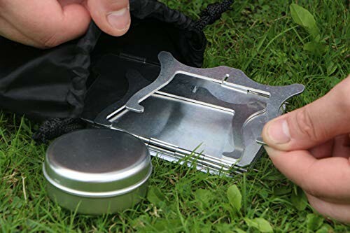 Hands assembling a portable camping stove on grass.