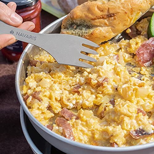 Scrambled eggs with bacon in a pan with a spork and bread.